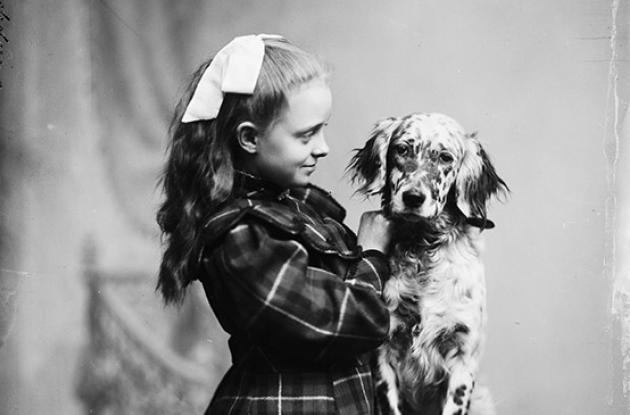 En flot klædt pige med sløjfe i håret står med en plettet hund
