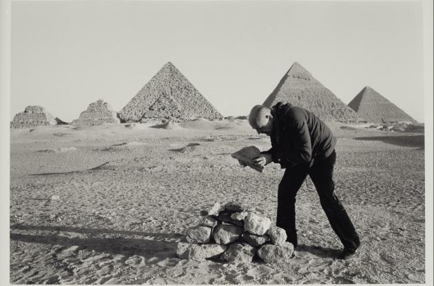 Mand bygger lille pyramide af sten foran pyramiderne i Egypten