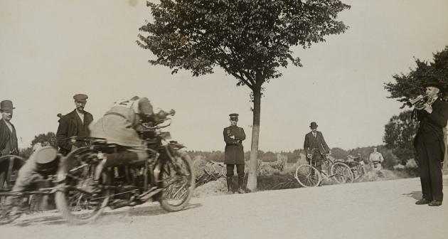 Mænd står på en vej og ser på en motorcykel med sidevogn køre forbi