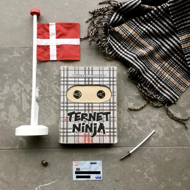 Bogen Ternet Ninja ligger på et gulv omringet af et dankort, et lille sværd og et Danmarksflag
