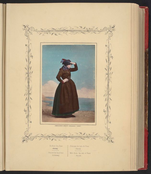 Et håndfarvet fotografi af en kvinde i en mørk nationaldragt er indsat i en side i en bog. Omkring fotografiet er tegnet en dekorativ ramme.