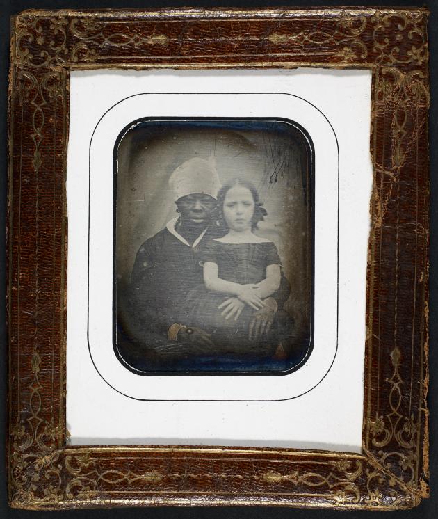 Et gammelt indrammet fotografi af en lille hvid pige med sin sorte amme